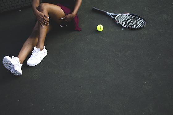 上图中，一位女士坐在网球拍和网球旁边，正在调整她的腿. 