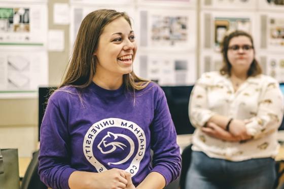 Photo of a smiling female student wearing a purple Chatham University shirt in a classroom.